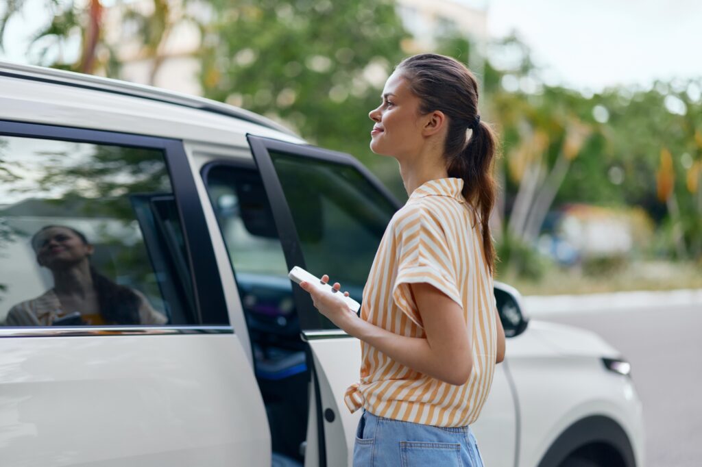 Woman with smartphone standing near a white van, dressed in casual attire, looking content in an